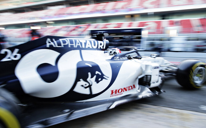 Close-up view of a speeding AlphaTauri Formula 1 race car with visible text including 'ALPHATAURI', '26', and 'HONDA' sponsorship branding, captured in motion blur on a racetrack pit lane. The image highlights the sleek design and branding of a high-performance racing vehicle, relevant for used cars and new cars enthusiasts interested in motorsport and automotive technology.