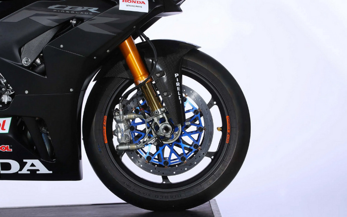 Close-up image of the front wheel and suspension of a black Honda CBR Fireblade motorcycle with branding including Honda Genuine Parts, Pirelli tyre, and Castrol stickers, highlighting detailed disc brakes and golden front forks, suitable for use in content about used cars and new cars.