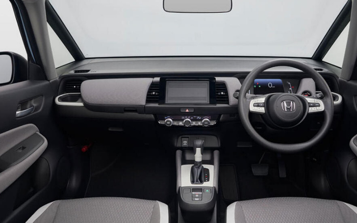 Interior dashboard view of a Honda car showing steering wheel with Honda logo, central touchscreen display, climate control knobs, gear shift, and two-tone grey seats. The image highlights the clean and modern design suitable for used cars and new cars buyers.