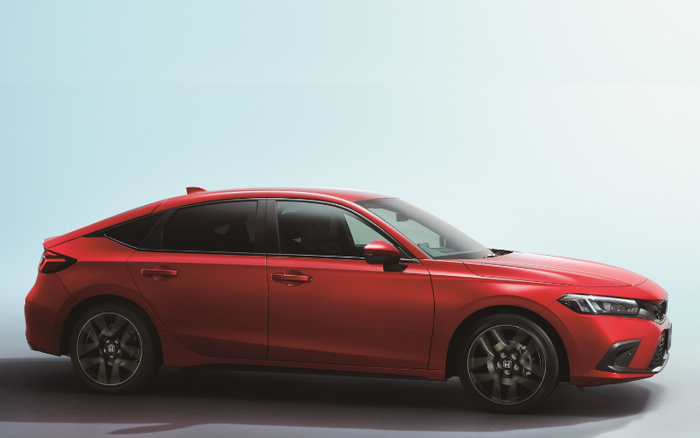 Side view of a shiny red modern Honda Civic hatchback car against a plain light background, showcasing sleek design and dark tinted windows, suitable for advertisements about used cars and new cars.