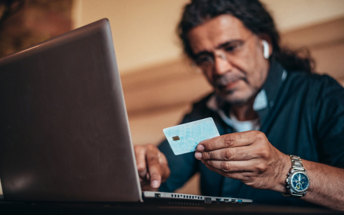 Man holding a credit card and using a laptop, possibly making an online purchase. The image conveys the concept of buying used cars or new cars online, highlighting secure digital transactions for vehicle purchases.