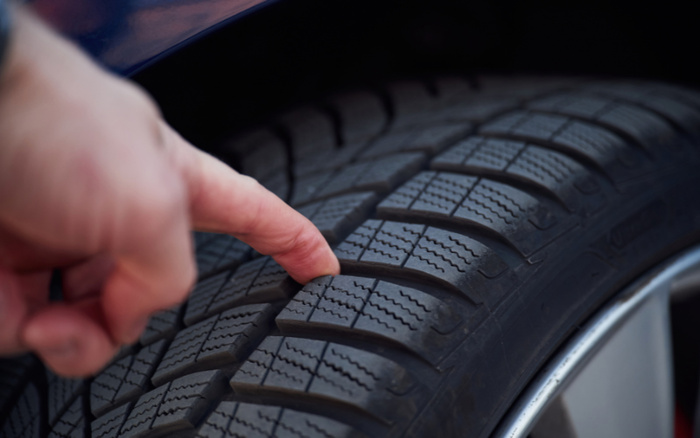 Close-up of a finger measuring the tread depth on a car tyre, illustrating the importance of tyre condition for used cars and new cars. The image highlights the detailed tread pattern on the tyre and the rim of the wheel.