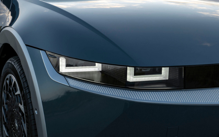 Close-up of the front left side of a dark blue car showing a modern, rectangular LED headlight with a distinctive illuminated pattern. The car has a sleek design with a smooth hood and a detailed wheel rim. The image highlights features relevant for both used cars and new cars car listings.