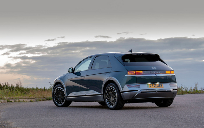 Rear and side view of a dark blue Hyundai Ioniq 5 electric car with registration plate ET21 JZW parked on a road at sunset, showcasing its modern design and illuminated rear lights, suitable for advertising used cars and new cars.