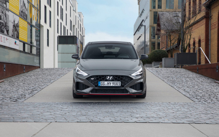 Front view of a grey Hyundai car with license plate GG HY 9001, parked on a modern cobblestone and concrete driveway between buildings in an urban setting. The image represents used cars and new cars in a city environment.