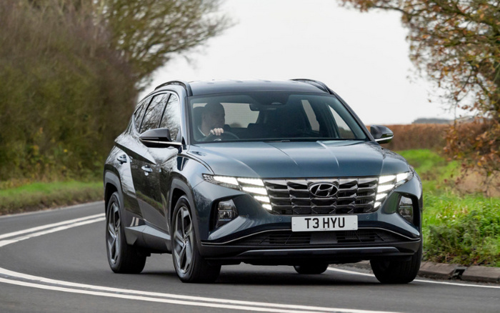 Grey Hyundai Tucson driving on a countryside road, showing distinctive front grille and LED daytime running lights, with UK license plate T3 HYU, suitable for used cars and new cars buyers seeking modern SUVs.