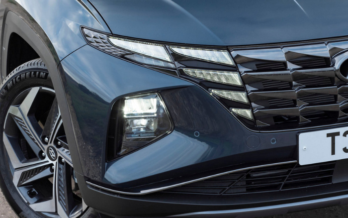 Close-up of the front left side of a dark blue Hyundai car featuring detailed headlight design with LED daytime running lights, a prominent black grille with Hyundai logo, and a Michelin tyre on an alloy wheel, showcasing a modern vehicle suitable for both used cars and new cars market.