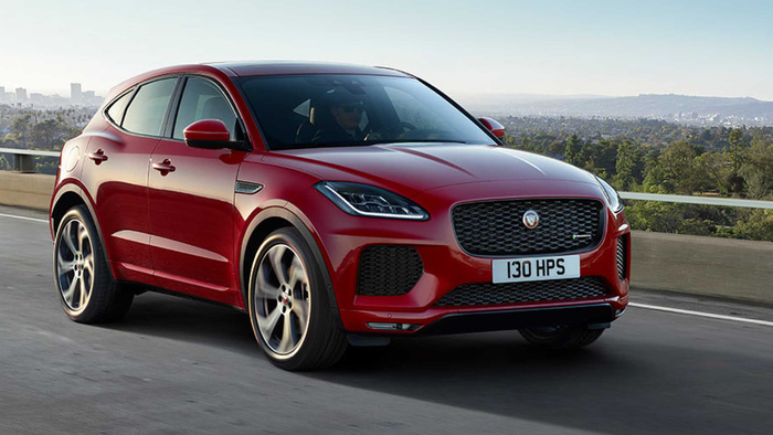 Red Jaguar SUV driving on a highway with city skyline and greenery in the background, car registration number 130 HPS visible on front plate, driver wearing sunglasses visible through tinted windows, sleek and modern car design representing both used cars and new cars.