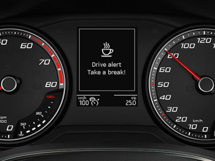 Car dashboard display showing speedometer and tachometer with a central alert screen displaying a steaming cup icon and the message 'Drive alert Take a break!'. Speedometer indicates approximately 110 km/h, tachometer around 2950 rpm, with additional data showing 100 km/h speed and 25.0°C temperature.