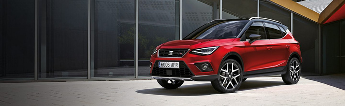 Red SEAT Arona car with registration plate 6006 AFR parked on a paved surface in front of large glass windows of a modern building, showcasing a sleek design perfect for both used cars and new cars buyers.