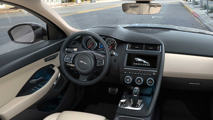 Interior view of a luxury Jaguar car showing the steering wheel with Jaguar logo, dashboard with speedometer and tachometer, centre console displaying the Jaguar logo on the screen, climate control dials showing temperatures of 19°C and 21°C, gear shifter, and beige leather seats. The image highlights the modern features and premium design typical of new cars, suitable for advertising used cars and new cars.