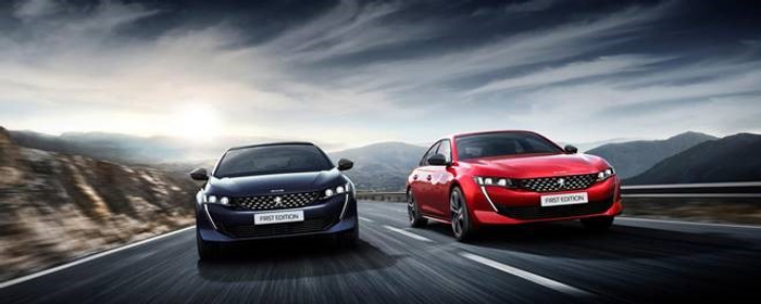 Two sleek Peugeot cars driving on a winding mountain road under a dramatic cloudy sky, one in deep blue and the other in red, both with 'FIRST EDITION' plates, representing high-quality new cars and appealing used cars.