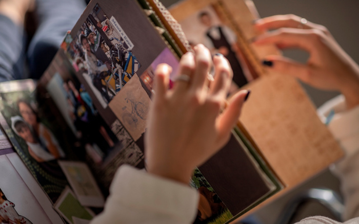 Person looking through a photo album with various photographs and sketches, including images of people and a drawing of a bicycle. The hands are focused on a framed photograph on the right side of the album. The background is blurred, and no text related to used cars or new cars is visible in the image.