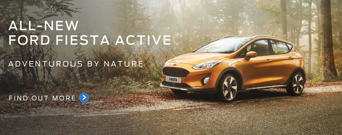Advertisement for the all-new Ford Fiesta Active car, shown in an orange colour parked on a leaf-covered road in a forest setting with trees and sunlight in the background. Text on the left side reads 'All-New Ford Fiesta Active', 'Adventurous by Nature', and 'Find Out More' with a blue arrow icon. The image promotes used cars and new cars, highlighting the adventurous character of the Ford Fiesta Active.