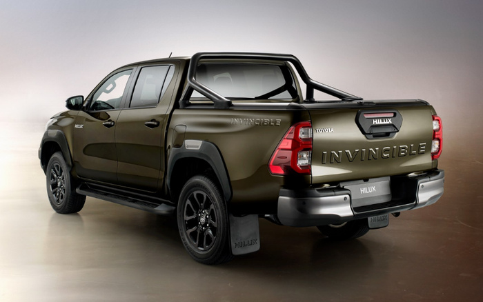 Rear side view of a dark green Toyota Hilux Invincible pickup truck with black alloy wheels, black roll bar, and visible Hilux and Invincible branding on the tailgate and side. The image showcases a clean, new car model in a studio setting, ideal for marketing used cars and new cars.