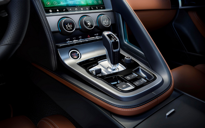 Close-up of a modern car's central console showing the gear shift lever, digital temperature controls displaying 19.5°C, AUTO, and 21.0°C settings, various buttons including START ENGINE STOP, and a touchscreen infotainment system above. The interior features black and brown leather with precise stitching, highlighting the premium design suitable for new cars and used cars.