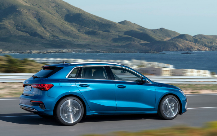 Blue Audi A3 Sportback 35 TFSI driving fast on a coastal road with mountains and water in the background, showcasing a sleek new car model ideal for buyers looking for used cars and new cars.