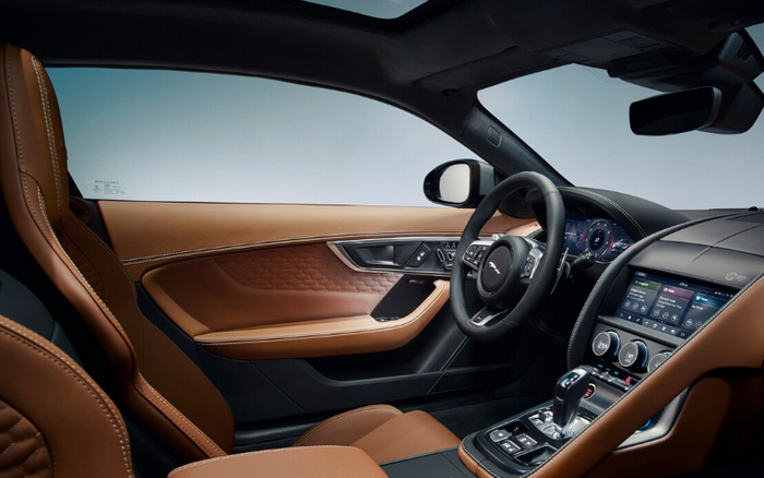 Interior view of a luxury car featuring tan leather seats and door panels with detailed stitching, a black leather-wrapped steering wheel displaying the Jaguar logo, and a digital dashboard with various controls. The centre console includes a touchscreen infotainment system, climate control dials, and a gear shifter, highlighting the premium design of new cars. The image showcases the high-end interior quality suitable for both used cars and new cars markets.