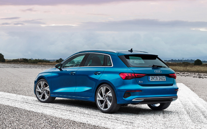 Blue Audi A3 hatchback parked on a gravel surface with a cloudy sky background, viewed from the rear left side. The car has a German license plate reading 'IN A 3401'. This modern vehicle represents new cars available on the market, ideal for customers interested in used cars or new cars options.
