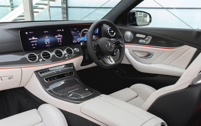 Interior of a new Mercedes-Benz car featuring a luxurious white and black leather design with carbon fibre trim. The dashboard includes a wide digital display showing car status, temperature, and multimedia options. The steering wheel has the Mercedes logo in the centre, with various control buttons. This modern, high-tech interior highlights features typical of new cars and is relevant for used cars buyers seeking premium models.