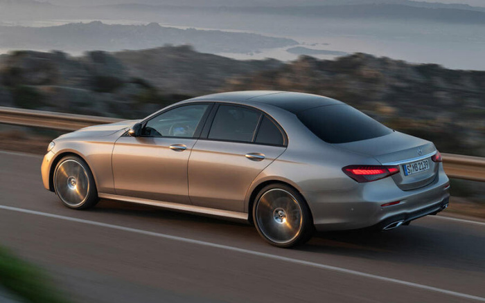 Silver Mercedes-Benz E-Class sedan driving on a coastal road with mountainous landscape in the background, displaying German license plate S MB 2439, representing a luxury new car model ideal for buyers interested in used cars or new cars.