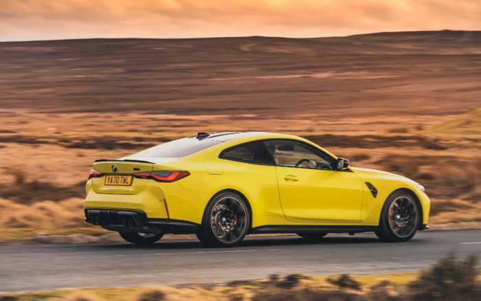 Yellow BMW M4 sports car driving on a road through a scenic countryside landscape during sunset, showcasing a sleek design and modern features, suitable as an example of luxury new cars and used cars available in the market.