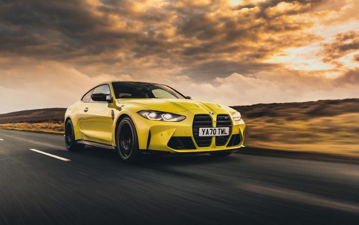 Yellow BMW M4 sports car driving on an open road during sunset with dramatic cloudy sky, UK license plate YA70 TML, showcasing sleek design and performance ideal for buyers interested in new cars or quality used cars.
