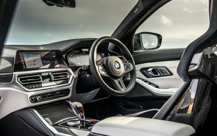 Interior view of a modern BMW car featuring a digital dashboard with navigation and media display, a multi-function steering wheel with BMW logo, carbon fibre trim accents, and a sporty bucket seat, highlighting features relevant for buyers interested in used cars and new cars.
