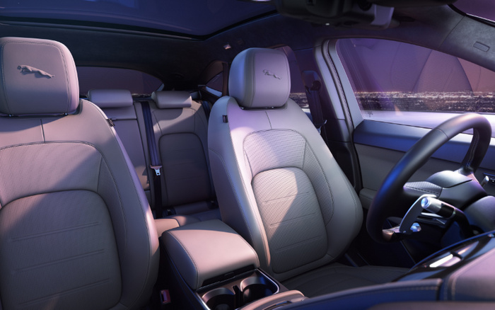 Interior view of a modern car featuring grey leather seats with Jaguar logo embossed on the headrests, centre console with cup holders, and a steering wheel on the right side, highlighting the luxurious design suitable for both used cars and new cars buyers.