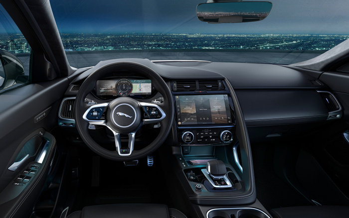 Interior view of a modern Jaguar car showcasing the digital dashboard, steering wheel with Jaguar logo, and centre console with touchscreen controls in a sleek black and metallic design, illustrating features typical of new cars available for sale alongside used cars.