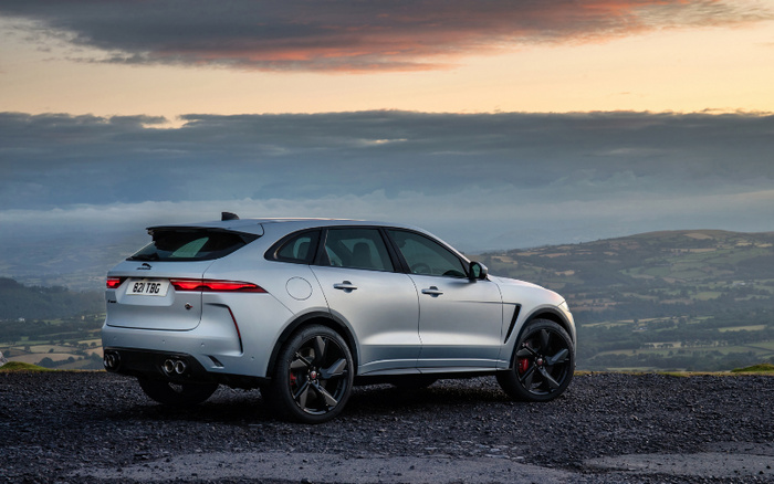 Silver Jaguar F-Pace SUV parked on a gravel road overlooking rolling green hills under a dramatic cloudy sunset sky, displaying the rear license plate 821 TBG, representing high-end used cars and new cars in scenic countryside surroundings.