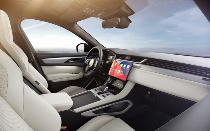 Interior of a modern car showcasing the driver's seat, steering wheel, and central console with a large touchscreen displaying app icons. The seats are upholstered in light cream leather with perforated detailing. The dashboard and door panels feature a combination of cream and black materials with sleek metallic accents. The view through the windows shows a clear sky and horizon, highlighting the clean and spacious design of the vehicle, ideal for promoting used cars and new cars.