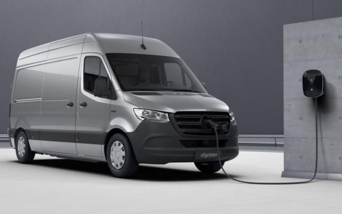 Silver Mercedes-Benz eSprinter electric van parked and charging at a wall-mounted charging station against a grey backdrop, representing new cars and electric vehicle technology, suitable for used cars and new cars market.
