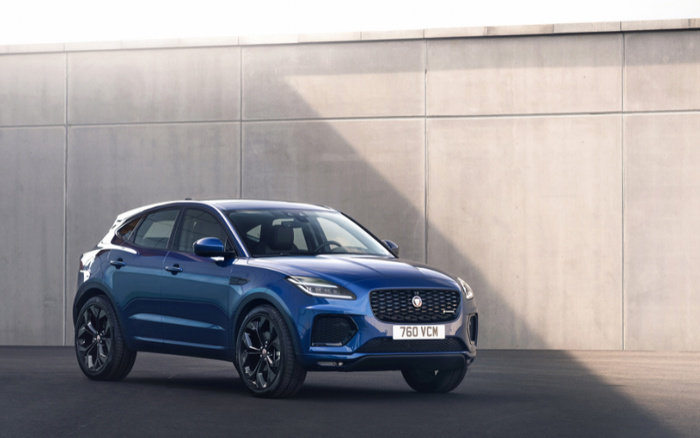 Blue Jaguar SUV parked in front of a large concrete wall with a shadow casting across it. The car has a license plate reading '760 VCM'. Image suitable for advertisements or listings of used cars and new cars.