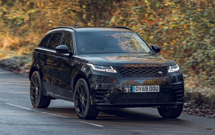 Black Range Rover Velar driving on a winding road with autumn foliage in the background, front view showing distinctive grille and LED headlights, registration plate OV69 OOU, suitable for used cars and new cars listings.
