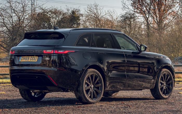 Black Range Rover Velar SUV parked on a gravel surface with trees and fencing in the background, featuring a UK license plate OV69 OOU, showcasing sleek design and black alloy wheels, suitable for advertising used cars and new cars.