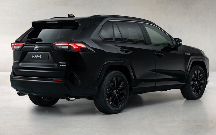 Black Toyota RAV4 Hybrid AWD parked indoors on a grey concrete floor and wall background, rear three-quarter view showing RAV4 badge, hybrid AWD badge, and sleek modern design with black alloy wheels, suitable for new cars and used cars market.