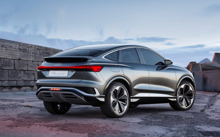 Silver Audi Q4 e-tron electric SUV parked on a rugged concrete surface near stone walls under a blue sky, rear three-quarter view showing sleek design and modern taillights, representing new cars and used cars options.