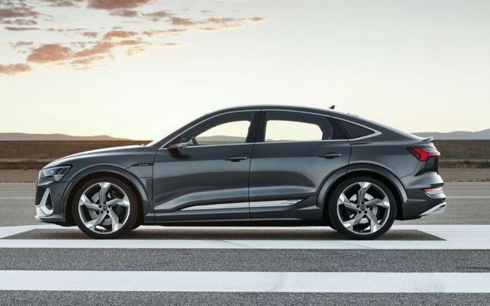 Side view of a sleek grey electric SUV parked on a zebra crossing with a sunset sky in the background, showcasing a modern design with sporty alloy wheels and aerodynamic lines, ideal for illustrating both used cars and new cars.