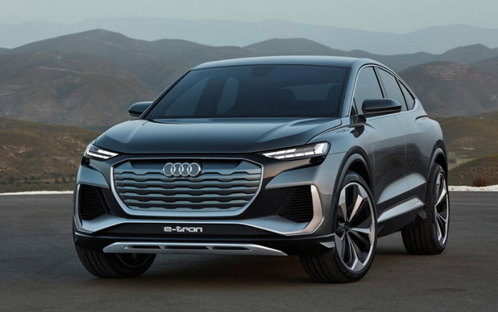 Front view of a sleek grey Audi e-tron electric SUV parked on a paved surface with mountainous landscape in the background, showcasing its modern grille design, LED headlights, and aerodynamic body, representing new cars and used cars options.