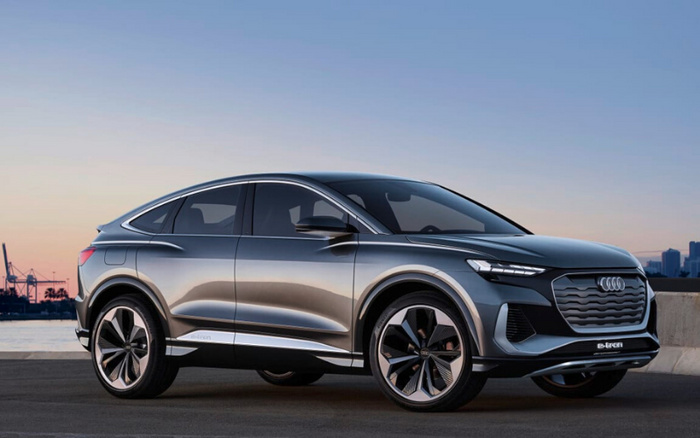 Sleek grey Audi e-tron electric SUV parked by a waterfront at sunset, showcasing modern design with large alloy wheels and distinctive front grille, representing a new car model suitable for buyers interested in used cars and new cars.