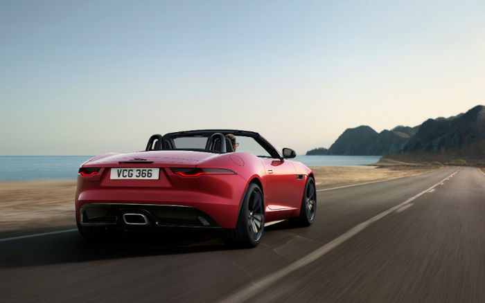 Red convertible sports car with the licence plate 'VCG 366' driving along a coastal road with the sea on the left and mountains in the distance, representing stylish new cars and used cars available for purchase.