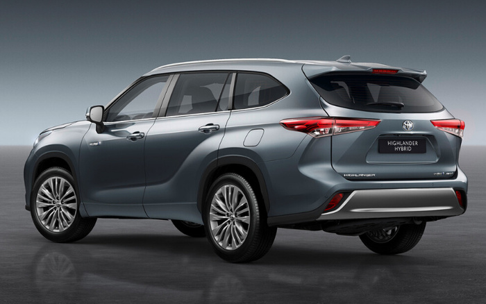 Rear side view of a grey Toyota Highlander Hybrid SUV on a reflective floor with a plain grey background, featuring modern rear lights and the badge reading 'HIGHLANDER HYBRID'. Suitable for used cars and new cars promotion.
