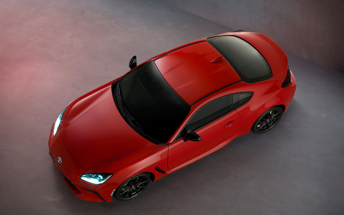 Top-down view of a shiny red sports car with sleek aerodynamic design, black roof, and headlights on, positioned on a smooth grey concrete floor, ideal for showcasing new cars or used cars in a showroom setting.