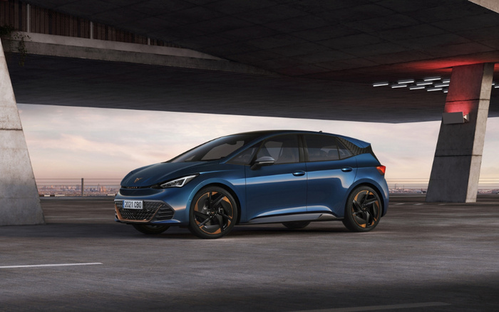 Blue 2021 Cupra Born electric hatchback car parked in a modern concrete parking structure with cityscape in the background, showcasing a sleek design with black and copper alloy wheels, highlighting a model suitable for both used cars and new cars buyers.