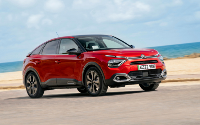 Red Citroën compact SUV driving on a coastal road with the sea and sandy beach in the background, license plate KZ22 VDK, showcasing a modern design ideal for used cars and new cars buyers.