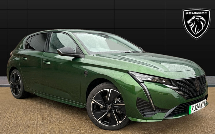 Green Peugeot 308 hatchback car with registration plate KJ24 MYA parked on a textured surface in front of a black tiled wall featuring a Peugeot lion logo. The image highlights a modern design of the new car model, suitable for used cars or new cars sales.