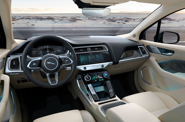 Interior view of a modern Jaguar car showcasing the steering wheel with Jaguar logo, digital dashboard displaying 'P 0', and dual touchscreen centre console controls. The beige leather seats and door trims contrast with the black dashboard and centre console. This image highlights the luxurious and high-tech features suitable for buyers interested in used cars or new cars.