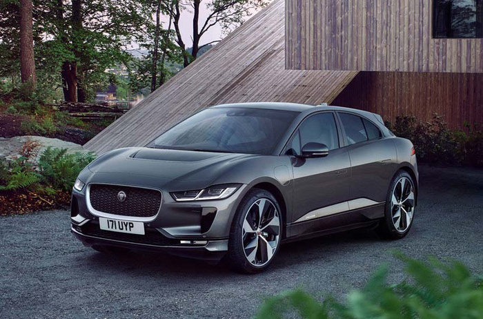 Grey Jaguar I-PACE electric car parked in front of a modern wooden house with a slanted roof, registration plate 171 UYP, surrounded by greenery and trees, ideal for used cars or new cars buyers looking for luxury electric vehicles.