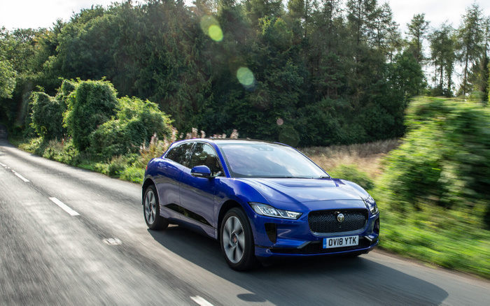 Blue Jaguar I-PACE electric car driving on a country road surrounded by green trees and bushes, registration plate OV18 YTK, representing new cars and used cars available.